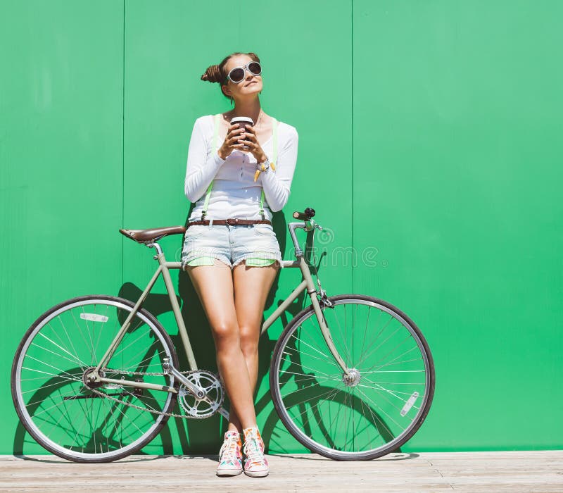 La bella giovane ragazza graziosa alla moda in breve ed i supporti degli occhiali da sole e della maglietta con la bicicletta rip fotografia stock La bella giovane ragazza graziosa alla moda in breve ed i supporti degli occhiali da sole e della maglietta con la bicicletta rip fotografia stock