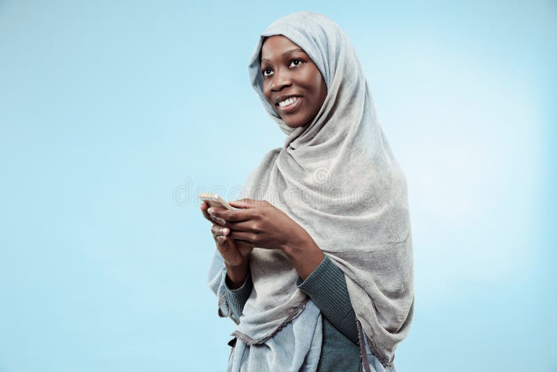 La bella giovane ragazza musulmana nera che indossa hijab grigio, con un sorriso felice sul suo fronte fotografia stock La bella giovane ragazza musulmana nera che indossa hijab grigio, con un sorriso felice sul suo fronte fotografia stock