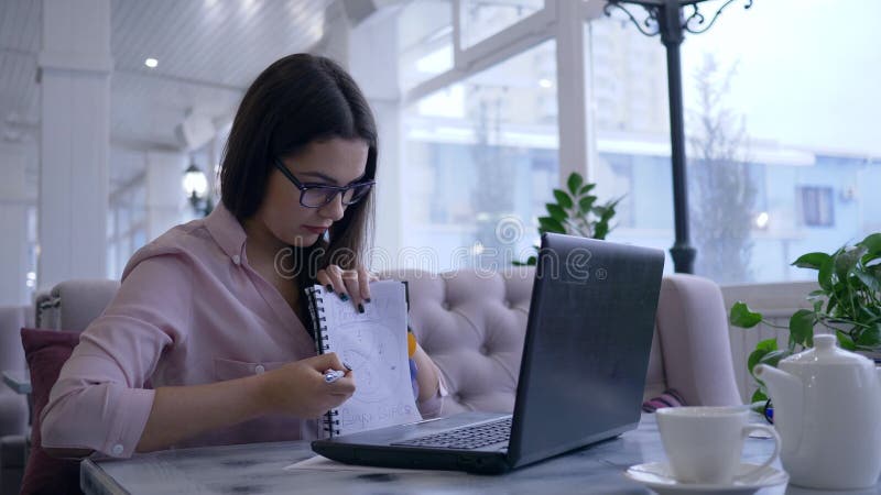 La bella ragazza astuta durante e-impara su video chiacchierata su netbook moderno mostra il blocco note con le note ed i sorrisi