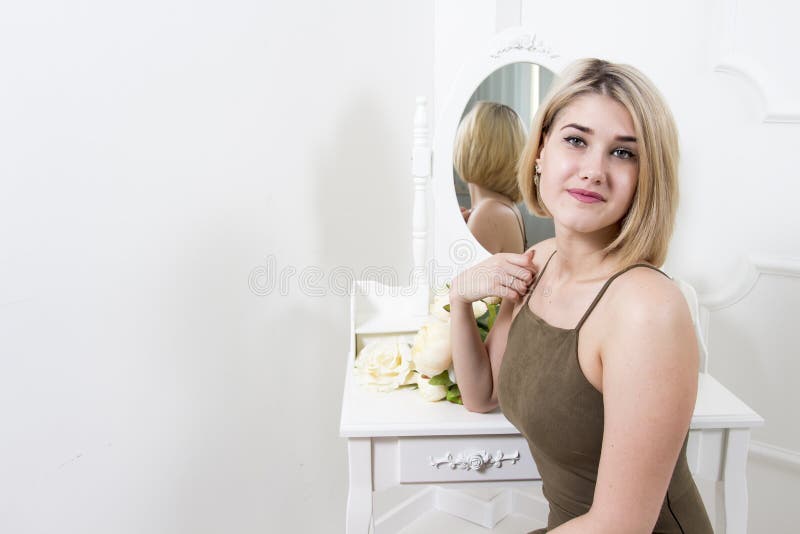 La bella ragazza bionda attraente si siede davanti ad uno specchio nella camera da letto Giovane donna nello spogliatoio immagine stock La bella ragazza bionda attraente si siede davanti ad uno specchio nella camera da letto Giovane donna nello spogliatoio immagine stock
