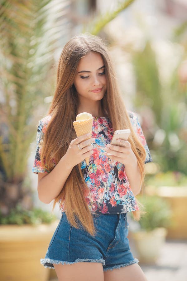 La bella ragazza con il gelato legge il messaggio sul telefono cellulare fotografia stock libera da diritti La bella ragazza con il gelato legge il messaggio sul telefono cellulare fotografia stock libera da diritti