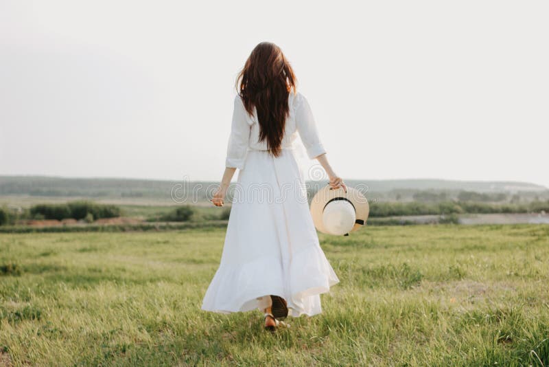La bella ragazza lunga spensierata dei capelli in vestiti e cappello di paglia bianchi gode della vita nel giacimento della natur immagini stock libere da diritti La bella ragazza lunga spensierata dei capelli in vestiti e cappello di paglia bianchi gode della vita nel giacimento della natur immagini stock libere da diritti