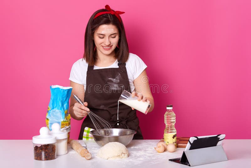 La belle femelle de brune verse le lait dans le plat Le chef malaxe la p?te, se pr?parant aux vacances de P?ques, faisant les pet photos libres de droits La belle femelle de brune verse le lait dans le plat Le chef malaxe la p?te, se pr?parant aux vacances de P?ques, faisant les pet photos libres de droits