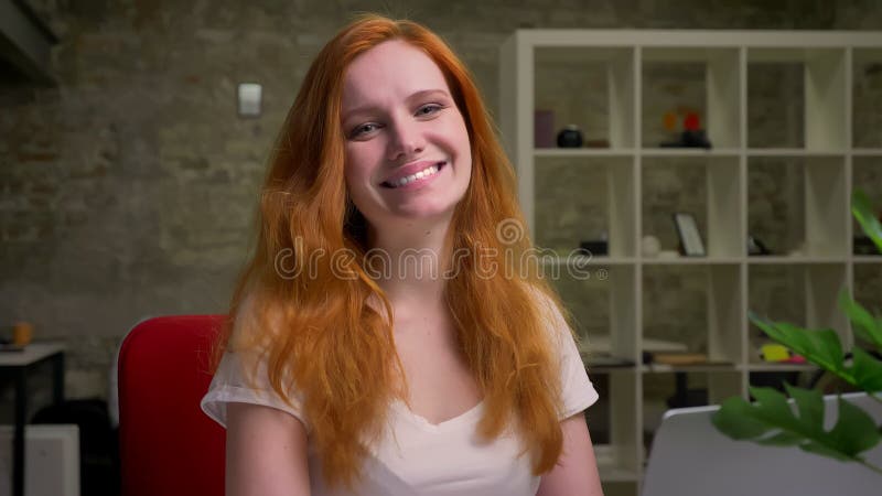 La belle femelle de gingembre sourit heureusement à la caméra tout en se reposant d'intérieur sur son lieu de travail dans le bur banque de vidéos