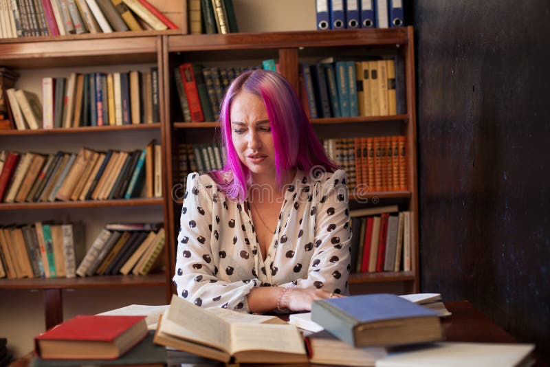 La belle femme avec les cheveux roses lit des livres dans la bibliothèque images libres de droits La belle femme avec les cheveux roses lit des livres dans la bibliothèque images libres de droits