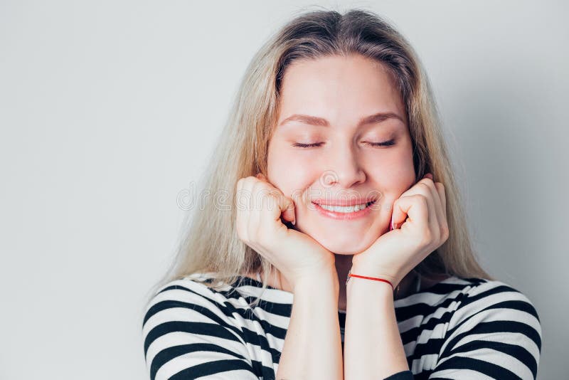 La belle femme blonde sourit et ferme ses yeux sur le fond blanc, plan rapproché Une jeune fille rêve et se réjouit images libres de droits La belle femme blonde sourit et ferme ses yeux sur le fond blanc, plan rapproché Une jeune fille rêve et se réjouit images libres de droits