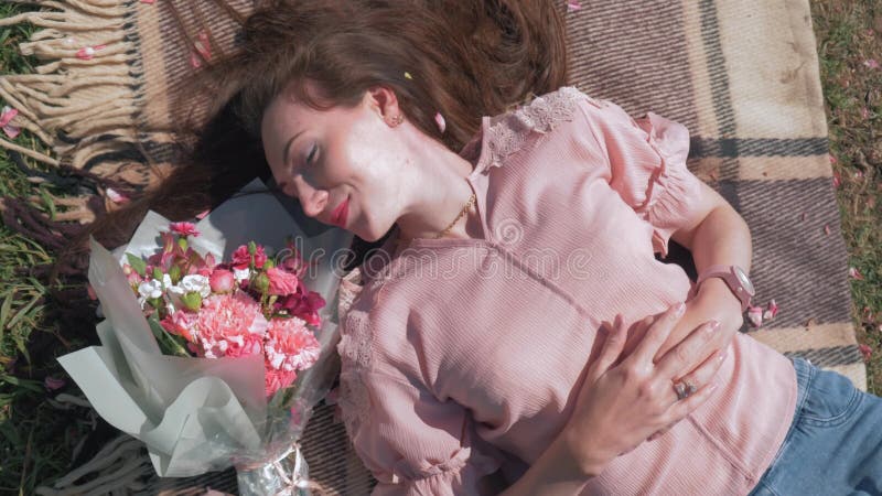 La belle femme heureuse se trouve près du beau bouquet des fleurs sur le couvre-lit sur la pelouse et apprécie la récréation exté