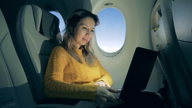 La belle femme travaille sur un ordinateur portable dans un avion au lever du soleil