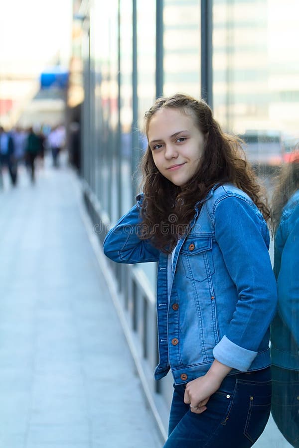 La belle fille de l'adolescence dans des vêtements de denim se tient se penchante sur un bâtiment en verre sur la rue de ville image libre de droits La belle fille de l'adolescence dans des vêtements de denim se tient se penchante sur un bâtiment en verre sur la rue de ville image libre de droits