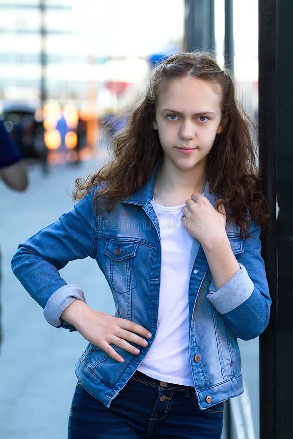 La belle fille de l'adolescence dans des vêtements de denim se tient se penchante sur un bâtiment en verre sur la rue de ville images stock La belle fille de l'adolescence dans des vêtements de denim se tient se penchante sur un bâtiment en verre sur la rue de ville images stock