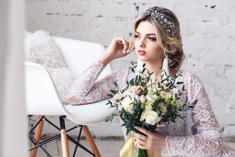 La belle fille habillée dans le peignoir et les sous-vêtements s'assied sur le plancher et tient le bouquet dans des ses mains images libres de droits La belle fille habillée dans le peignoir et les sous-vêtements s'assied sur le plancher et tient le bouquet dans des ses mains images libres de droits