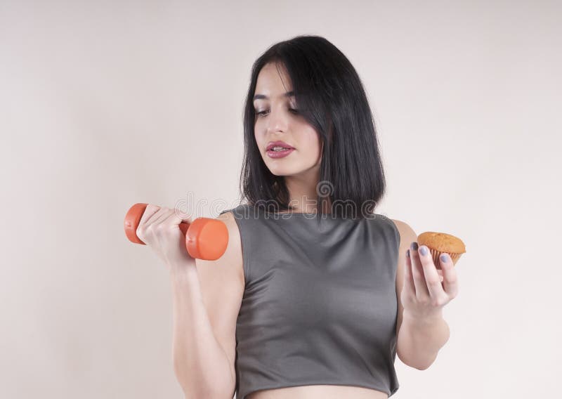 La belle haltère et le gâteau de jeune fille de sports équilibrent le studio de choix de formation de measuringexpression image stock La belle haltère et le gâteau de jeune fille de sports équilibrent le studio de choix de formation de measuringexpression image stock