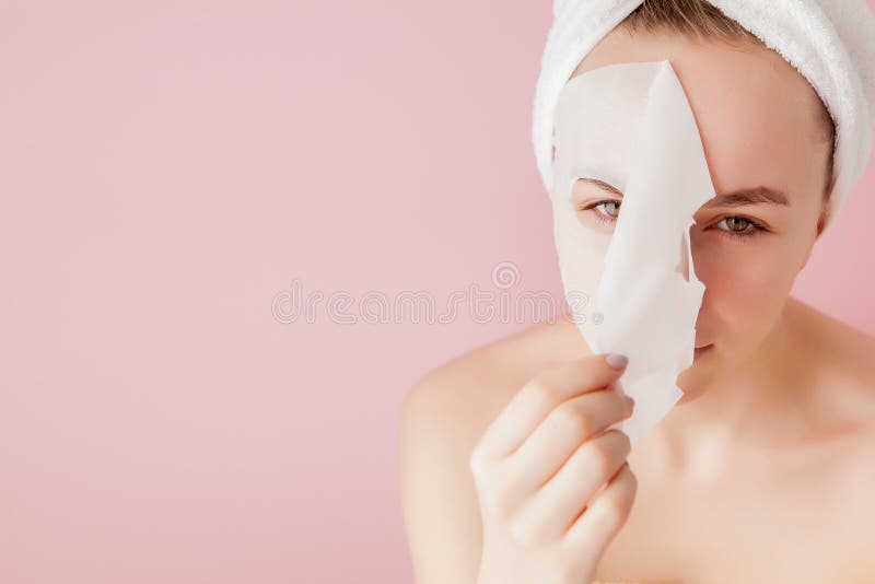 La belle jeune femme applique un masque cosm?tique de tissu sur un visage sur un fond rose Traitement de soins de sant? et de bea photo stock La belle jeune femme applique un masque cosm?tique de tissu sur un visage sur un fond rose Traitement de soins de sant? et de bea photo stock
