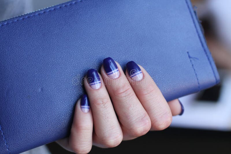 La belle main femelle avec la manucure tient l'embrayage en cuir Vernis à ongles bleu-foncé avec la conception créative photographie stock La belle main femelle avec la manucure tient l'embrayage en cuir Vernis à ongles bleu-foncé avec la conception créative photographie stock
