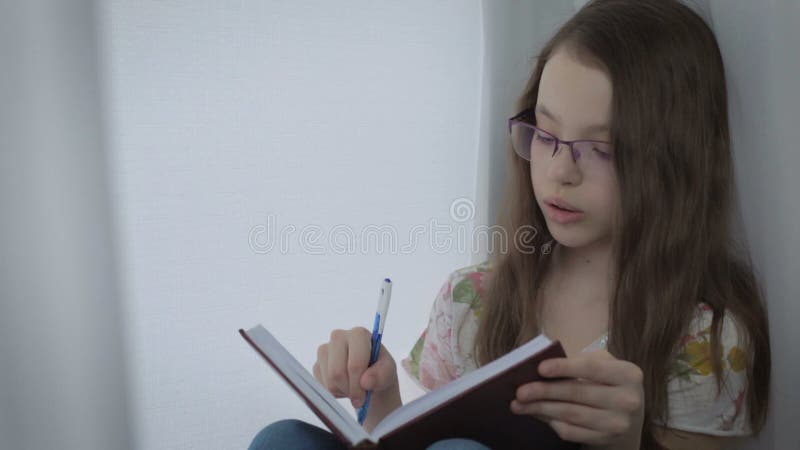 La belle petite fille avec des verres se dicte et a écrit en journal intime