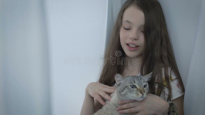 La belle petite fille communique doucement avec votre chat aimé à la fenêtre