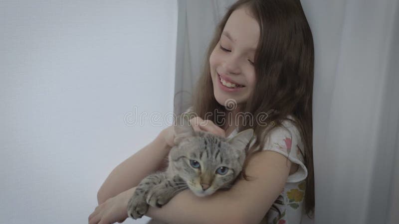 La belle petite fille communique doucement avec votre chat aimé à la fenêtre