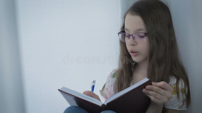 La belle petite fille en verres fait diligemment son travail à la fenêtre