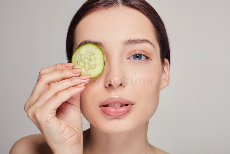 La bellissima ragazza dai capelli castani con le labbra piene e la calma completa le tiene in mano una fetta di cetriolo vicino a fotografie stock libere da diritti La bellissima ragazza dai capelli castani con le labbra piene e la calma completa le tiene in mano una fetta di cetriolo vicino a fotografie stock libere da diritti
