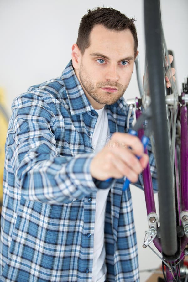 La bici della riparazione dell'uomo spinge dentro il deposito fotografia stock La bici della riparazione dell'uomo spinge dentro il deposito fotografia stock