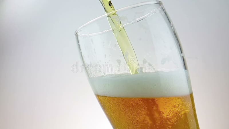 La birra fresca di versamento con schiuma nel vetro della pinta della bevanda con ghiaccio congelato cade, sparato il movimento l
