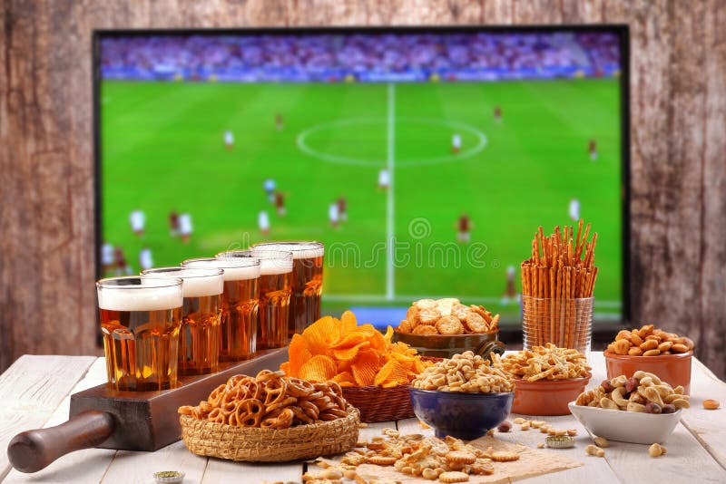La bière et les casse-croûte ont placé sur le fond du match de football TV photographie stock
