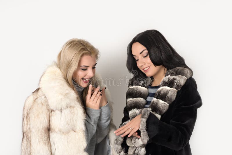 La blonde et le brunett de deux amies dans des manteaux de fourrure courts observent un r images stock La blonde et le brunett de deux amies dans des manteaux de fourrure courts observent un r images stock