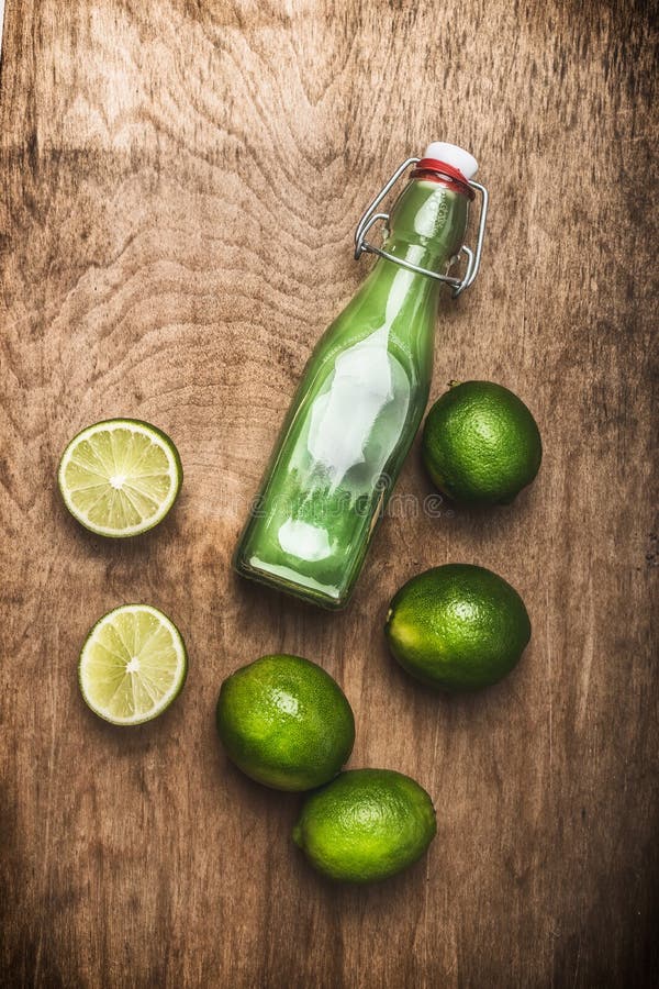 La botella de zumo de lima con la cal fresca da fruto en el fondo de madera rústico, visión superior foto de archivo La botella de zumo de lima con la cal fresca da fruto en el fondo de madera rústico, visión superior foto de archivo