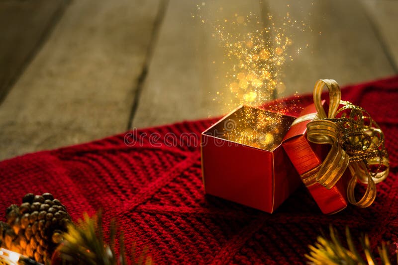 Red Christmas gift box on red scraf with gold particles light magical on wooden desk. Red Christmas gift box on red scraf with gold particles light magical on wooden desk.