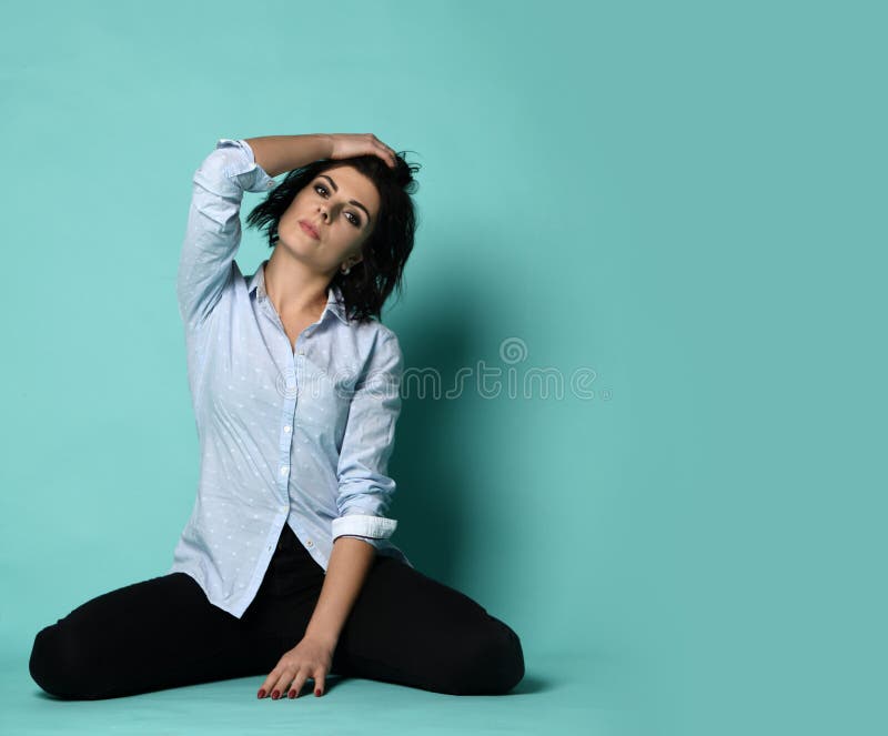 La casalinga della giovane donna in camicia blu-chiaro sembra stanca e si siede sul pavimento immagine stock La casalinga della giovane donna in camicia blu-chiaro sembra stanca e si siede sul pavimento immagine stock