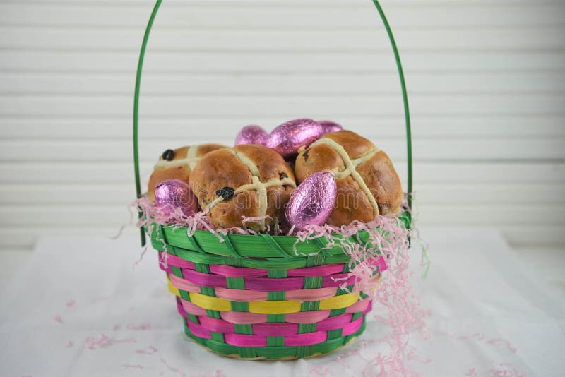 La cesta de Pascua llenó de los bollos cruzados calientes frescos y de los huevos rosados brillantes imagen de archivo libre de regalías La cesta de Pascua llenó de los bollos cruzados calientes frescos y de los huevos rosados brillantes imagen de archivo libre de regalías
