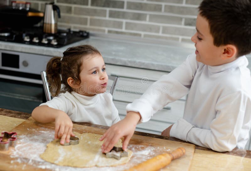 La chica es lipthral mirando a su hermano. Los niños preparan las galletas de Navidad en su cocina fotografía de archivo