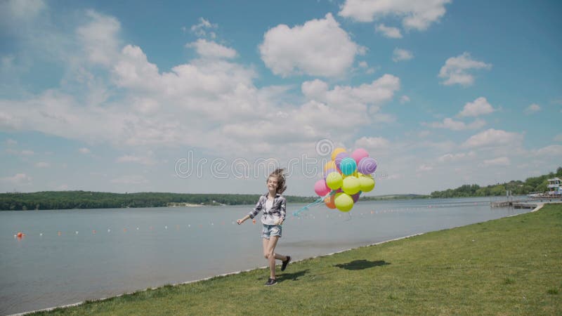 La chica joven bonita corre con los globos a disposición en el coustline metrajes