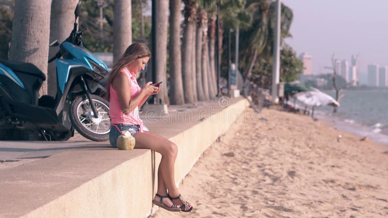 La chica joven con el pelo largo se sienta en el parapeto hace el selfie