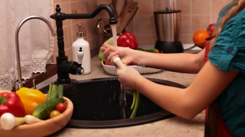 La chica joven da verduras que se lavan en el fregadero de cocina