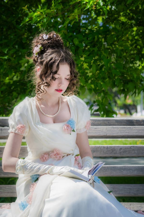 La chica joven está leyendo un libro que se sienta en un banco foto de archivo libre de regalías La chica joven está leyendo un libro que se sienta en un banco foto de archivo libre de regalías
