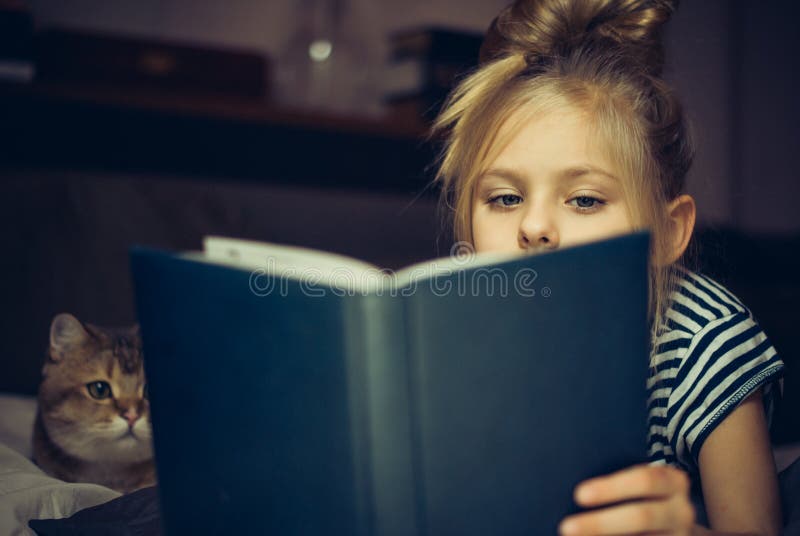 Young girl reads book to a cat in bed. Young girl reads book to a cat in bed