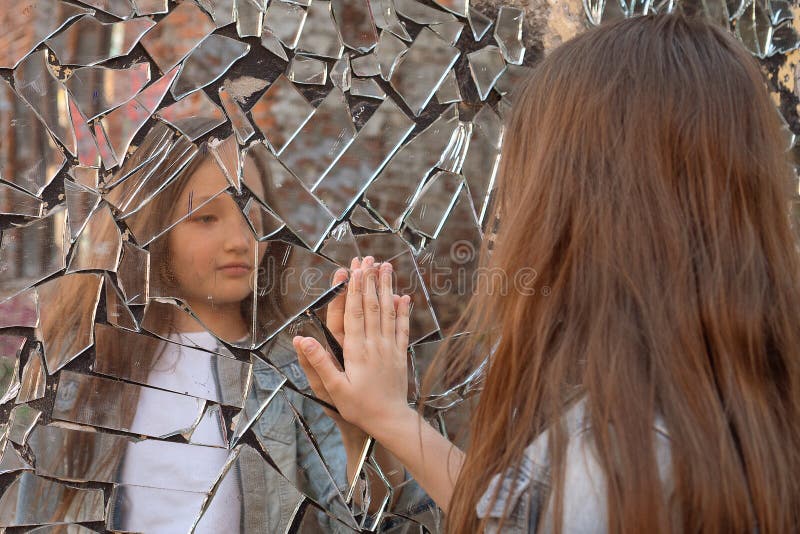 Young girl looks in a broken mirror and shows her hand on a mirror. Young girl looks in a broken mirror and shows her hand on a mirror