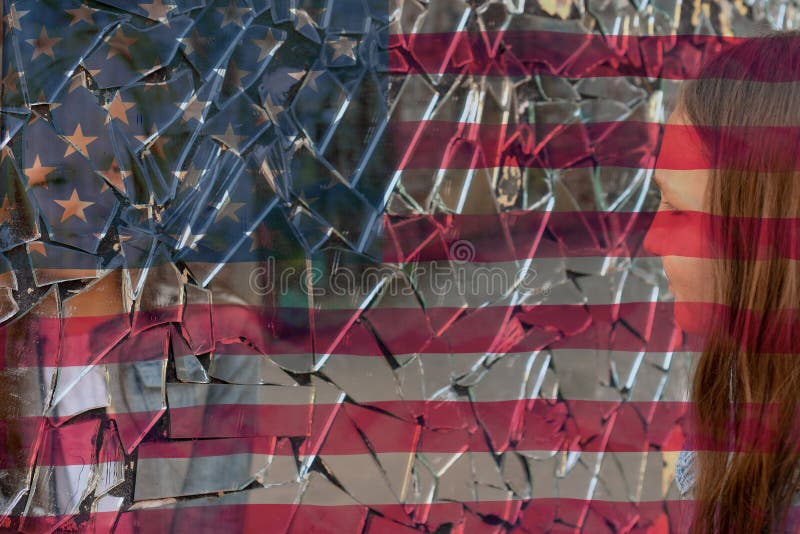 Young girl looks in a broken mirror and shows her hand on a mirror against the background of the American flag. Young girl looks in a broken mirror and shows her hand on a mirror against the background of the American flag.