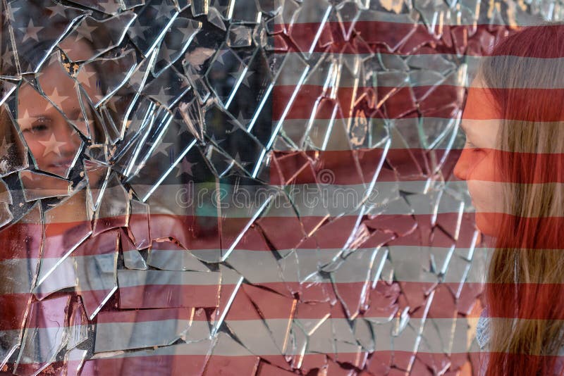 Young girl looks in a broken mirror and shows her hand on a mirror against the background of the American flag. Young girl looks in a broken mirror and shows her hand on a mirror against the background of the American flag.