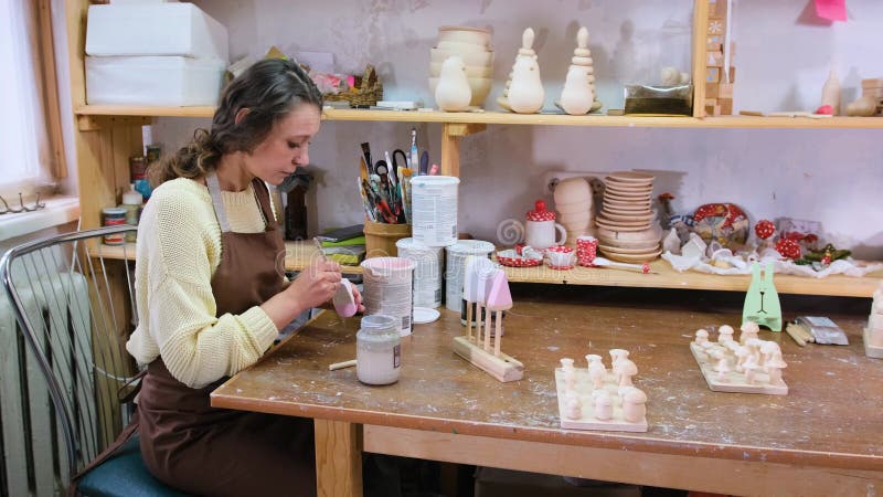 La chica maestro pinta juguetes de madera con pinturas acrílicas. producción de juguetes ecológicos para niños almacen de video