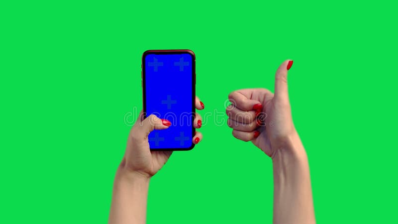 La chica sostiene un teléfono con una pantalla azul en el cromakey y le da un pulgar hacia arriba. una mujer con una manicura roja