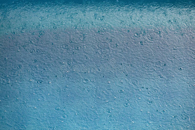 La chute de gouttes de pluie dans la piscine. Englobe des bulles et des touches sur la surface de l'eau. La pluie arrose. Texture de la surface de l'eau avec des gouttes. Vue de dessus