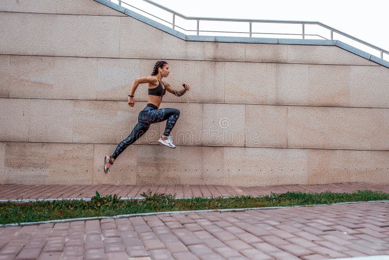 La ciudad hermosa del verano de los tatuajes de la chica joven funciona con el salto que escucha el smartphone disponible música imagen de archivo libre de regalías La ciudad hermosa del verano de los tatuajes de la chica joven funciona con el salto que escucha el smartphone disponible música imagen de archivo libre de regalías