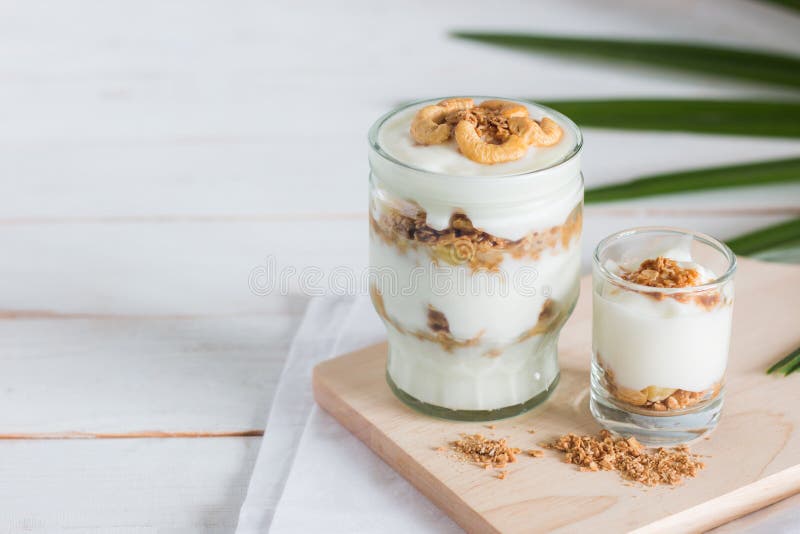 La comida sana hecha del granola en vidrio, el yogur y los copos de maíz adornan la comida con el ajuste del anacardo en tabla de fotografía de archivo libre de regalías La comida sana hecha del granola en vidrio, el yogur y los copos de maíz adornan la comida con el ajuste del anacardo en tabla de fotografía de archivo libre de regalías