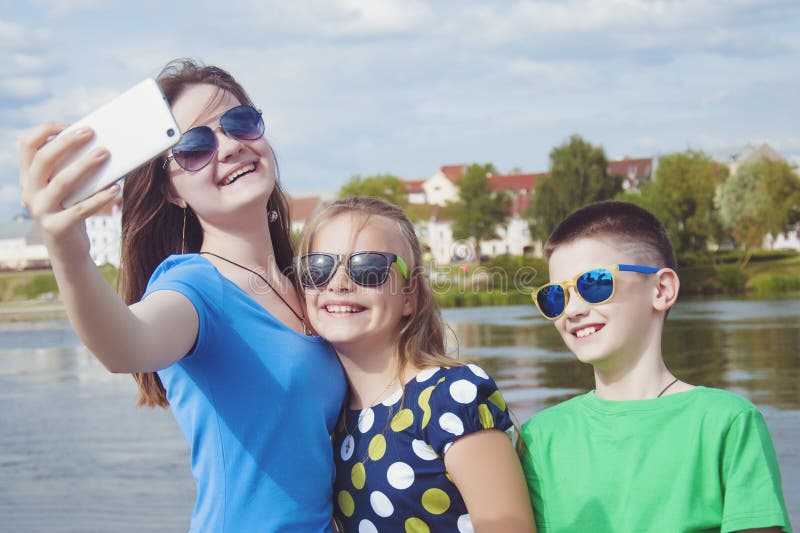 La compañía alegre del ` s de los niños hace el selfie en un smartphone en una calle de la ciudad al aire libre fotografía de archivo libre de regalías La compañía alegre del ` s de los niños hace el selfie en un smartphone en una calle de la ciudad al aire libre fotografía de archivo libre de regalías