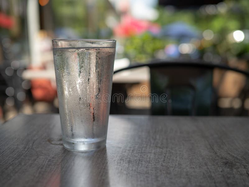 La condensazione ha coperto il bicchiere d'acqua che si siede fuori su una tavola scura