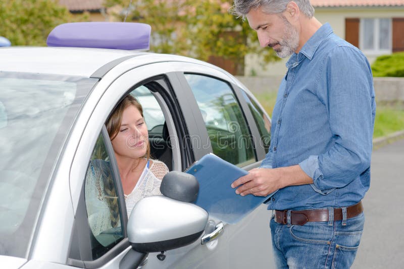 La conducción del profesor de escuela se colocaba fuera del coche que hablaba con el principiante femenino imagen de archivo libre de regalías La conducción del profesor de escuela se colocaba fuera del coche que hablaba con el principiante femenino imagen de archivo libre de regalías