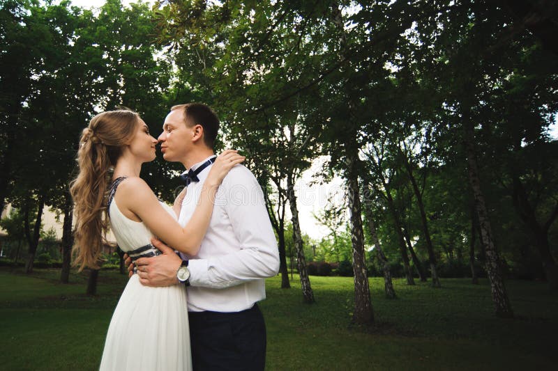 La coppia in abbigliamento di nozze è nelle mani contro il contesto del campo al tramonto, alla sposa ed allo sposo fotografia stock La coppia in abbigliamento di nozze è nelle mani contro il contesto del campo al tramonto, alla sposa ed allo sposo fotografia stock
