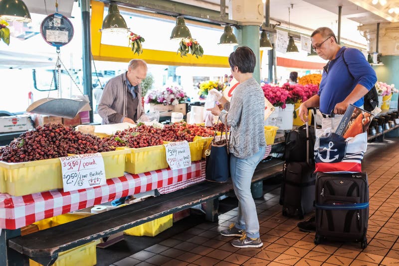 Seattle, WA, June 4, 2016: Shopping couple talk with cherries vendor at Pike Place Market. Seattle, WA, June 4, 2016: Shopping couple talk with cherries vendor at Pike Place Market